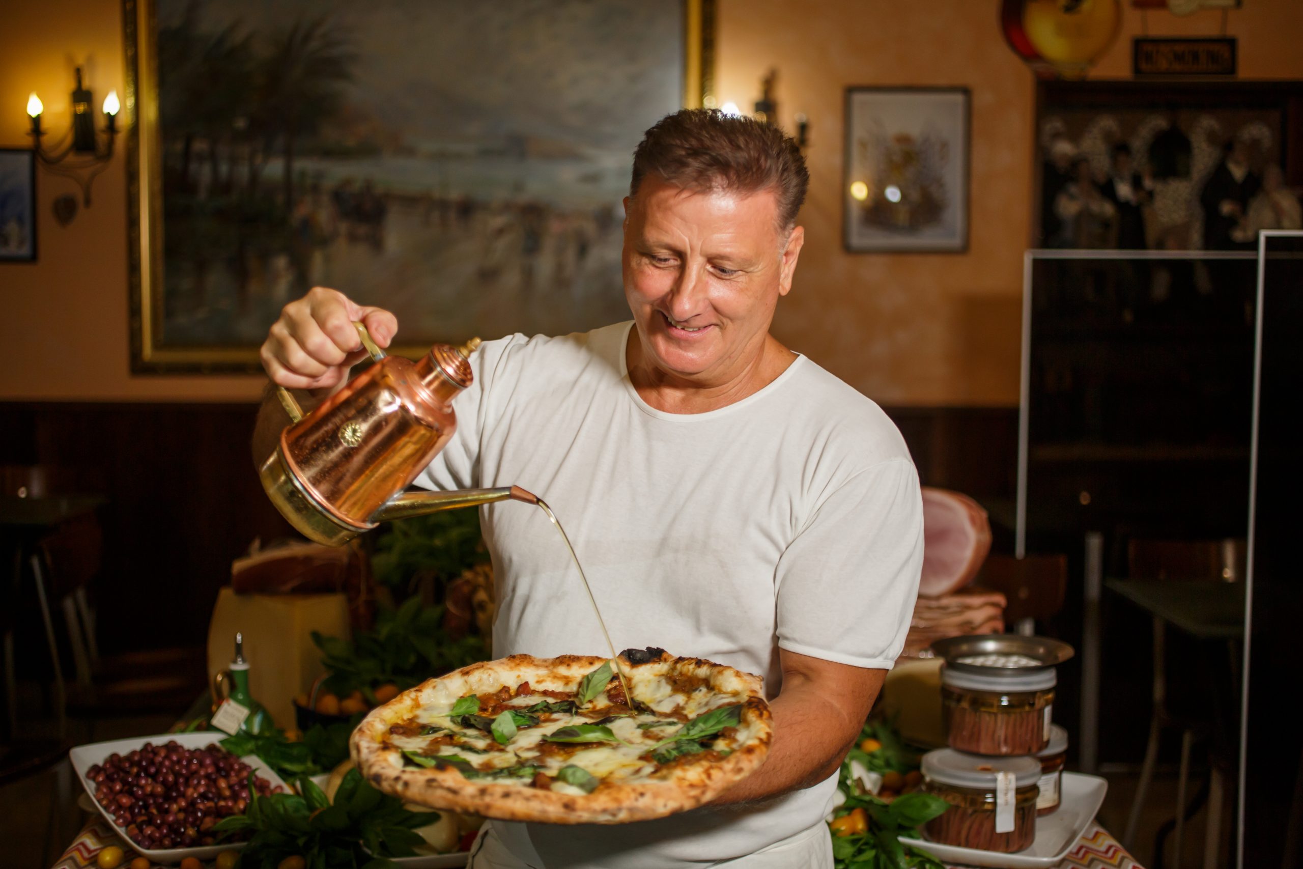 Man pouring olive oil on pizza