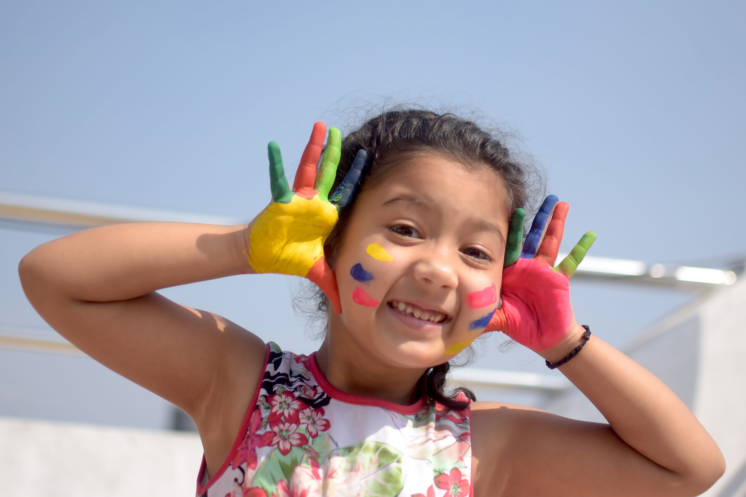 A child from Nepal. She is holding her hands up by her face. Her hands are painted pink, yellow, green, and blue.