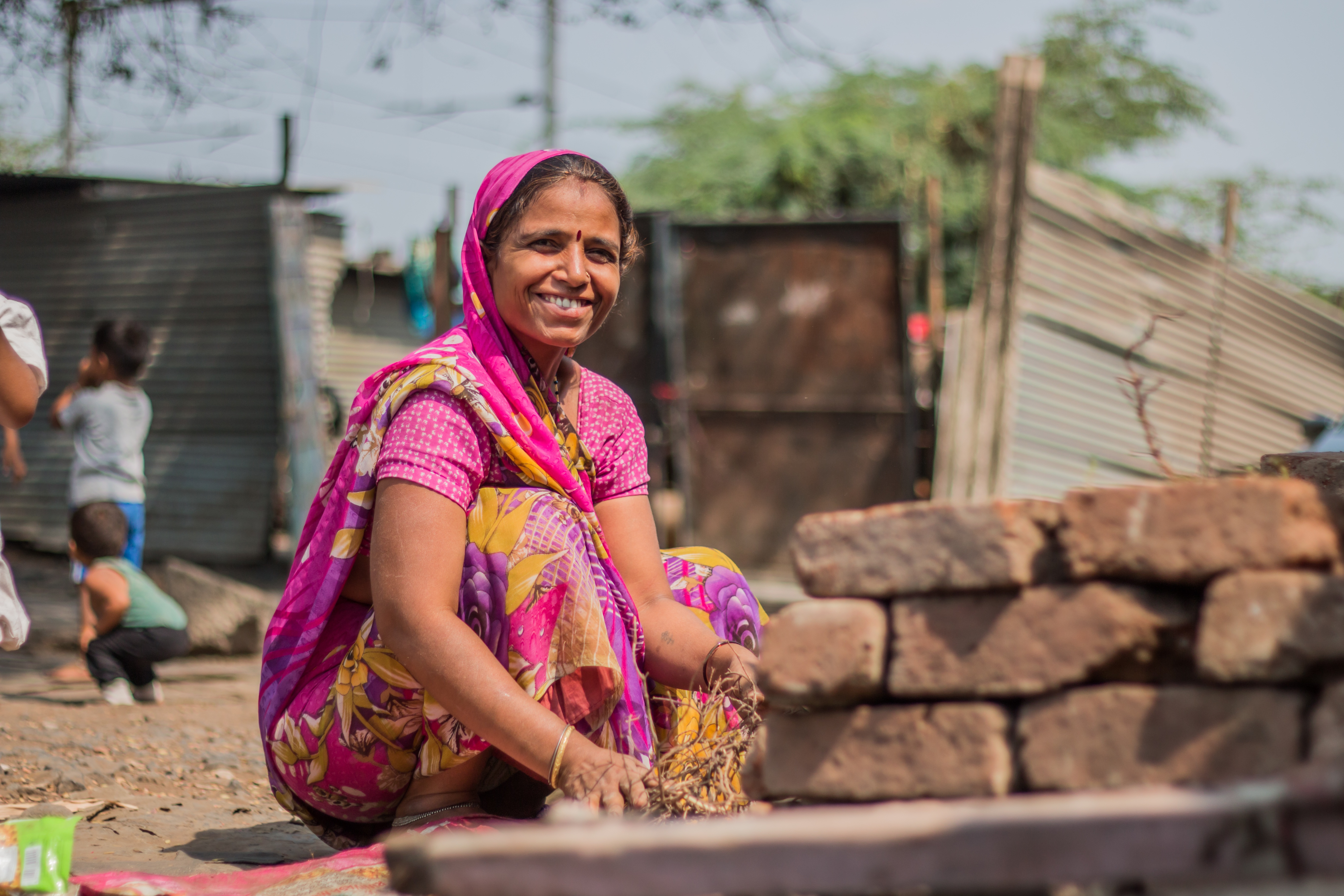 A woman in India. She is wearing a pink robe and is smiling.