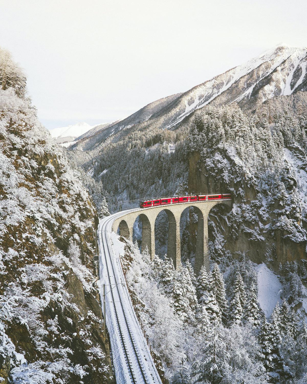 A train on a bridge in the snowy mountains