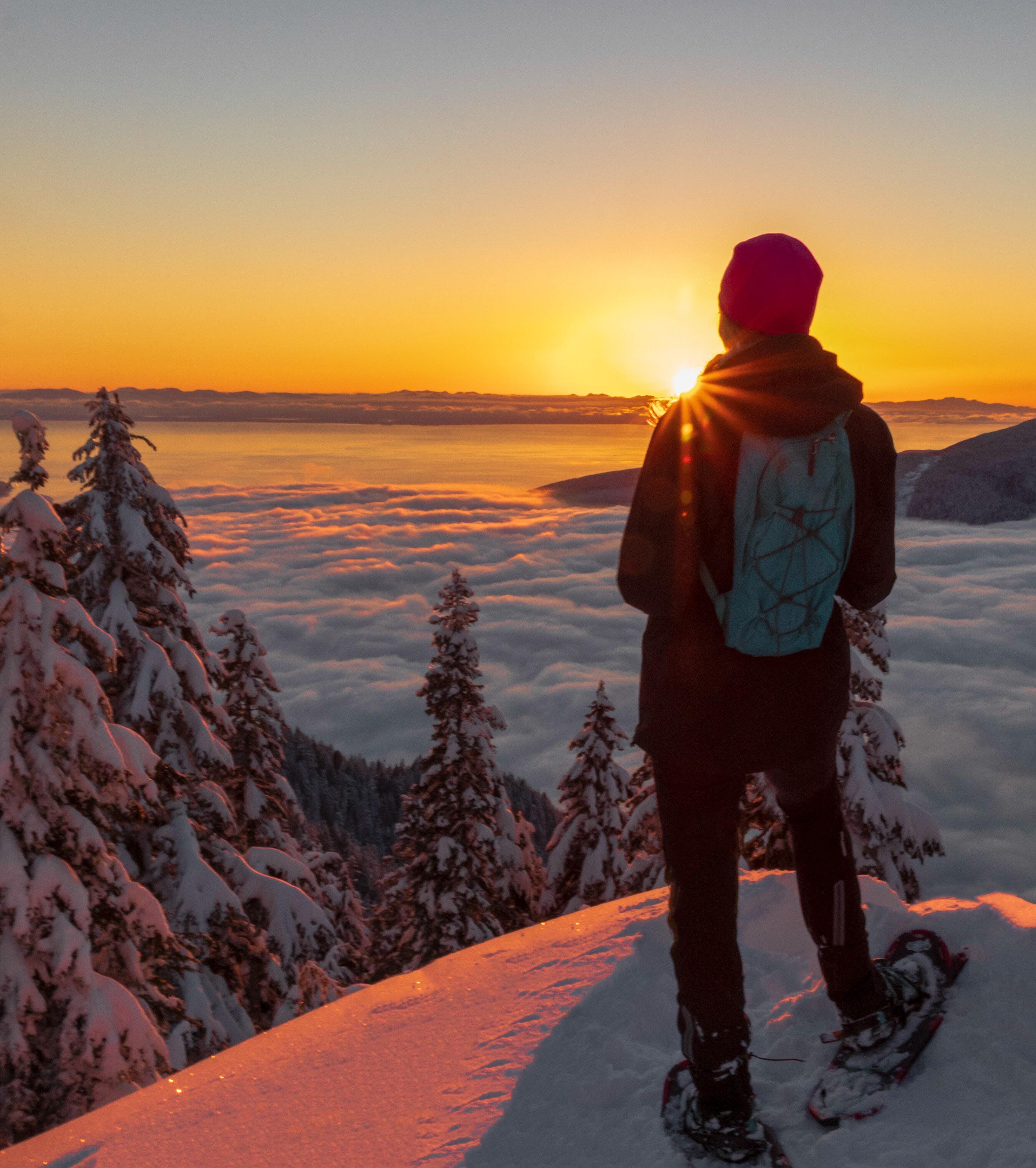 A person who snowshoed to the top of a mountain and is looking at the sunset